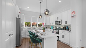 Een moderne keuken met witte kasten, een centraal eiland met barstoelen, een magnetron en een rookvrij-bord.