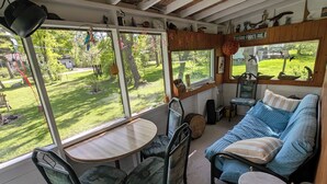 Ein gemütliches Interieur mit Holzbalkendecke, einem großen Fenster mit Blick auf einen grünen Garten, einer Couch und einem Esstisch mit Stühlen.