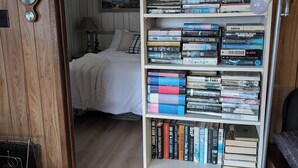 Ein Zimmer mit einer Bücherwand voller Bücher, einem Bett mit weißer Bettwäsche, einer Lampe und einer Holztür mit einer Uhr.
