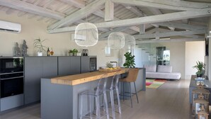 Una cocina moderna con una isla central, taburetes de bar y un comedor con sofá y mesa de centro.