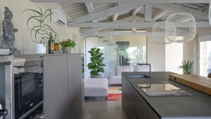 Una cocina moderna con horno integrado, una isla grande con pileta y un comedor con sofá blanco y alfombra colorida.