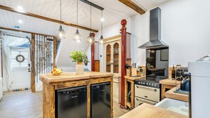 A kitchen with wooden cabinetry, a built-in dishwasher, a stove, and hanging pendant lights. - The B Hive at Buckstone House (Carnforth)