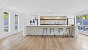 A modern kitchen with a central island, bar stools, and a large window. - Black Shack Burleigh (Burleigh Waters)