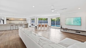 A modern living room with a white sofa, a dining area, and a kitchen. - Black Shack Burleigh (Burleigh Waters)
