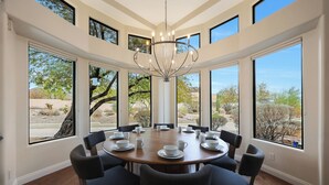 Un'ampia sala da pranzo con un tavolo rotondo apparecchiato per otto persone, grandi finestre con vista sul paesaggio desertico e un lampadario moderno.