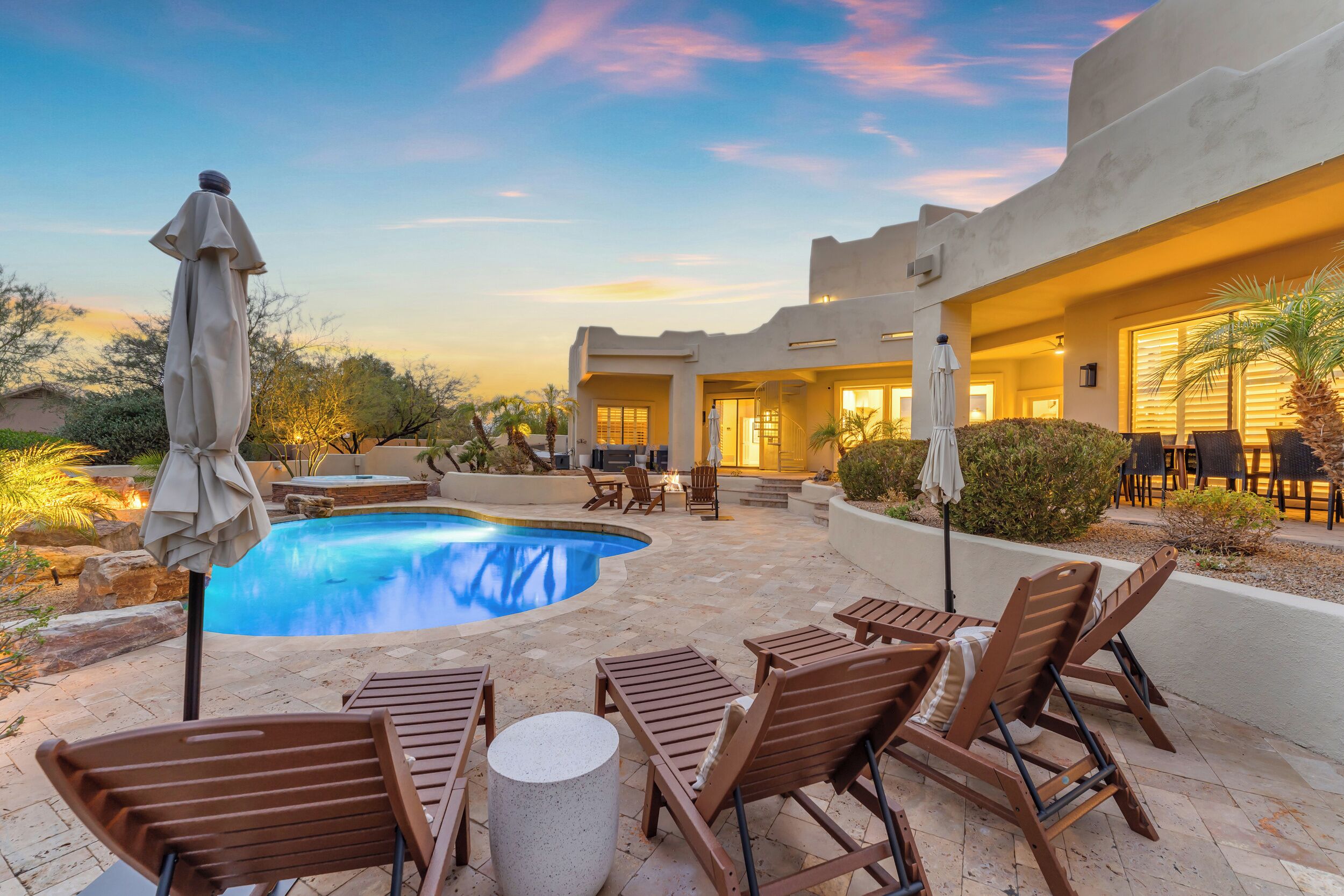 A pool area with lounge chairs and a table, surrounded by a building with a patio.