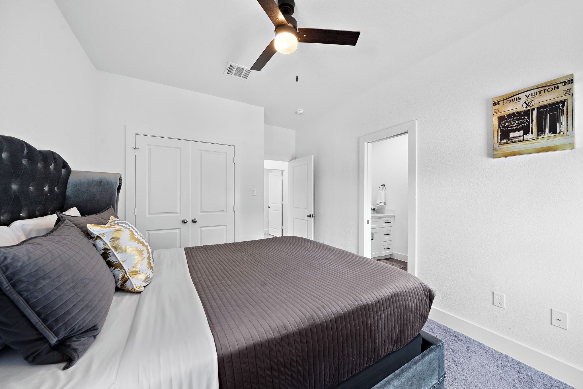 Ein Schlafzimmer mit einem Bett, Deckenventilator, weißen Wänden und einer Tür.