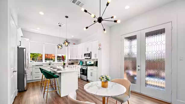 A modern kitchen with white cabinets, a central island, and a dining area with a round table and chairs. - Cozy Home Near MedCenter, Uptown, & Downtown (Houston)