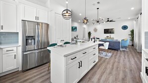 A modern kitchen with white cabinetry, a stainless steel refrigerator, and a central island with a sink. - Cozy Home Near MedCenter, Uptown, & Downtown (Houston)