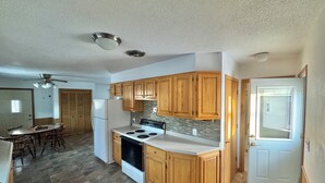 A kitchen with wooden cabinets, a white refrigerator, a stove, and a dining area with a table and chairs. - Private Lakeside Escape on Devils Lake  (Devils Lake)