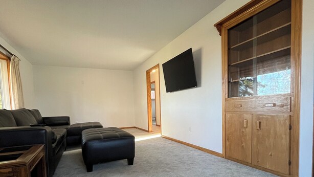 A living room with a sectional sofa, an ottoman, a wooden cabinet, and a flat-screen TV mounted on the wall. - Private Lakeside Escape on Devils Lake  (Devils Lake)