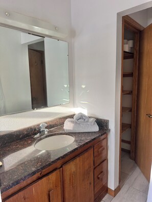 A bathroom with a marble countertop, a sink, a mirror, wooden cabinets, and a wooden door leading to a closet. - Private Lakeside Escape on Devils Lake  (Devils Lake)
