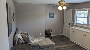 A cozy living room with a gray sectional sofa, a ceiling fan, a small stool, and a window with blinds. - Cozy B- condo in charming Corpus Christi with WiFi, AC near Laguna Madre (Corpus Christi)