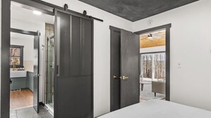 A modern bedroom with a large bed, a sliding door to a bathroom, and a view of a balcony. - Cozy 4-Bedroom Modern Mountaintop Retreat in Jewett  (Jewett)