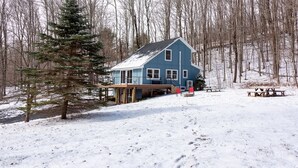A blue house with a deck, surrounded by snow-covered ground and leafless trees. - Cozy 4-Bedroom Modern Mountaintop Retreat in Jewett  (Jewett)