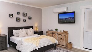 A modern bedroom with a bed, bedside tables, a TV, and a wall-mounted air conditioner. - Spacious Studio Retreat (Phoenix)