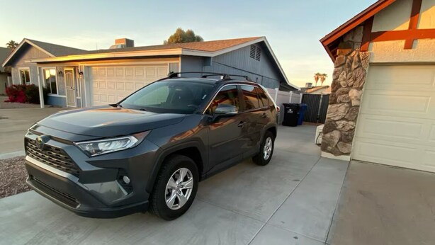 A gray SUV parked in a driveway with a garage and a house in the background. - Spacious Studio Retreat (Phoenix)