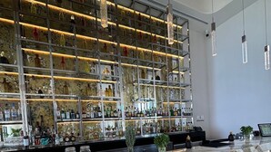 Una zona de bar con mostradores de mármol, estantes llenos de botellas de licor y lámparas colgantes.