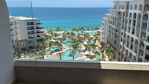 Un balcón con vistas a la piscina de un resort, palmeras y un edificio con varios balcones.