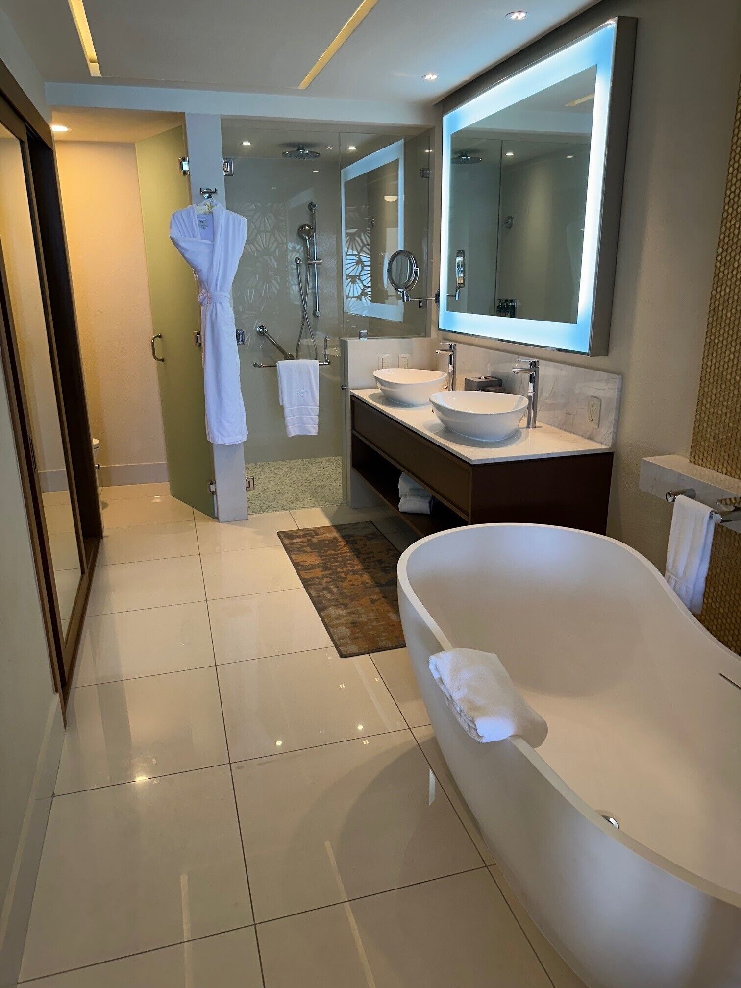 Ein modernes Badezimmer mit einer großen Badewanne, zwei Waschbecken, einer Glasdusche und einem großen Spiegel.