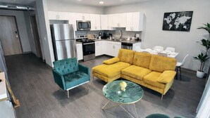 Una sala de estar moderna con un sofá amarillo, sillones color turquesa y una mesa de centro de vidrio.