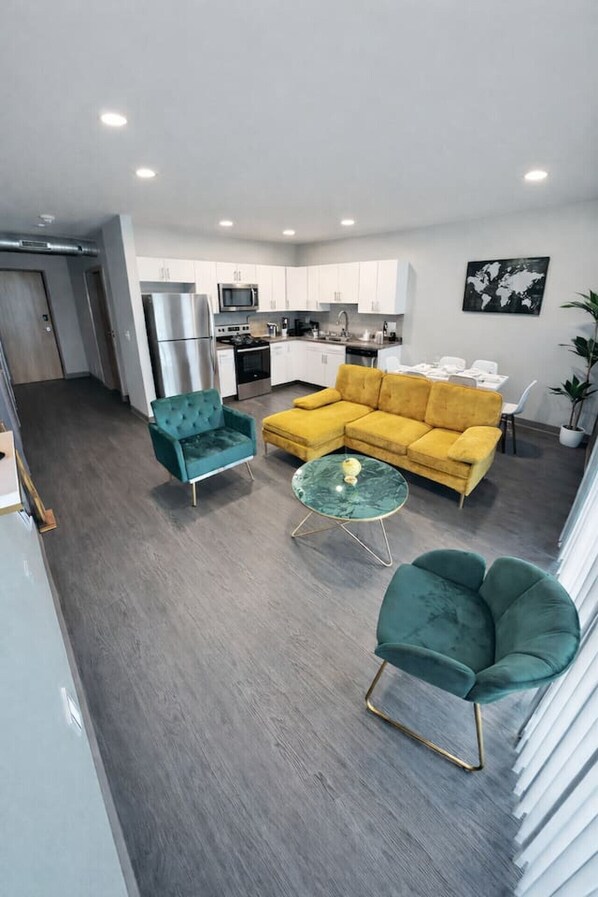 Un salon moderne avec un canapé jaune, des fauteuils turquoise et une table basse en verre.