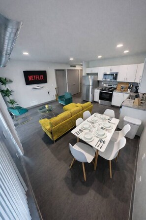 Un appartement moderne comprenant un coin repas, un canapé jaune, une cuisine et un téléviseur affichant le logo de Netflix.