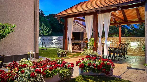 A covered outdoor seating area with a stone fireplace, surrounded by potted plants and a stone wall. - Amazing home in Lucane (Lucane)
