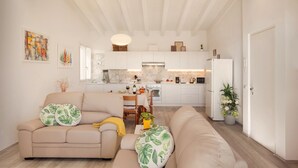 A modern living room with a beige sofa, a dining table, and a kitchen in the background. - White Apartment with Terrace and Lake View (Costermano)