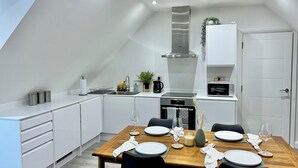 Eine moderne Küche mit weißen Schränken, einer Edelstahl-Dunstabzugshaube und einem Essbereich mit einem Holztisch, gedeckt für vier Personen.