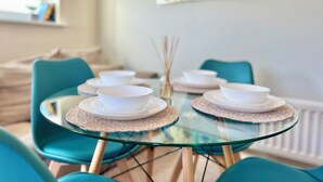 Una mesa de comedor con cuencos y platos blancos, rodeada de sillas color turquesa, en una habitación moderna con un cuadro abstracto grande en la pared.