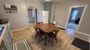 A dining area with a wooden table and chairs, a ceiling fan, and a kitchen with a sink and cabinets.