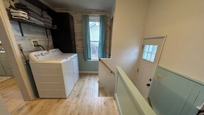 A laundry room with a washing machine and dryer, wooden floors, a window with curtains, and a door with a light switch.
