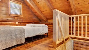 Een slaapkamer in een houten blokhut met een stapelbed, een raam met zonwering, en een houten ladder.