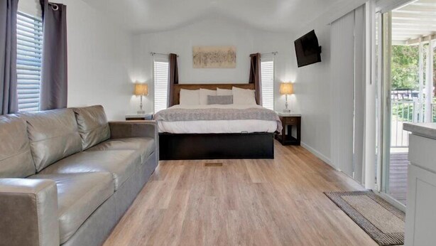 A bedroom with a bed, a sofa, two bedside lamps, a ceiling fan, and a TV on the wall. - Cozy 1BR Cottage Retreat near Dollywood (Pigeon Forge)