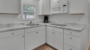 A kitchen with white cabinets, a microwave, a sink, and a window with blinds. - Cozy 1BR Cottage Retreat near Dollywood (Pigeon Forge)