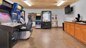 Ein Zimmer mit Holzboden und -wänden, ausgestattet mit Spielautomaten, einem Fernseher und einer Theke mit verschiedenen Gegenständen.