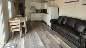 Un espacio habitable compacto con kitchenette, comedor y zona de estar con sofá.