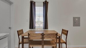Une salle à manger avec une table en bois et quatre chaises, une fenêtre avec des stores et une porte.