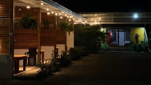 Un bâtiment moderne doté d’un espace extérieur couvert avec des sièges, de guirlandes lumineuses et d’un jardin bien entretenu.