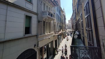 Une rue étroite bordée de bâtiments des deux côtés, une tour qui se profile au loin et quelques piétons.