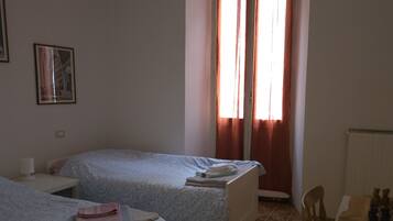 A room with two single beds, a table with a chess set, a hanging light, and a window with curtains.