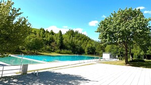 Ein Schwimmbad mit klarem, blauem Wasser, umgeben von Bäumen und einem gepflasterten Weg.