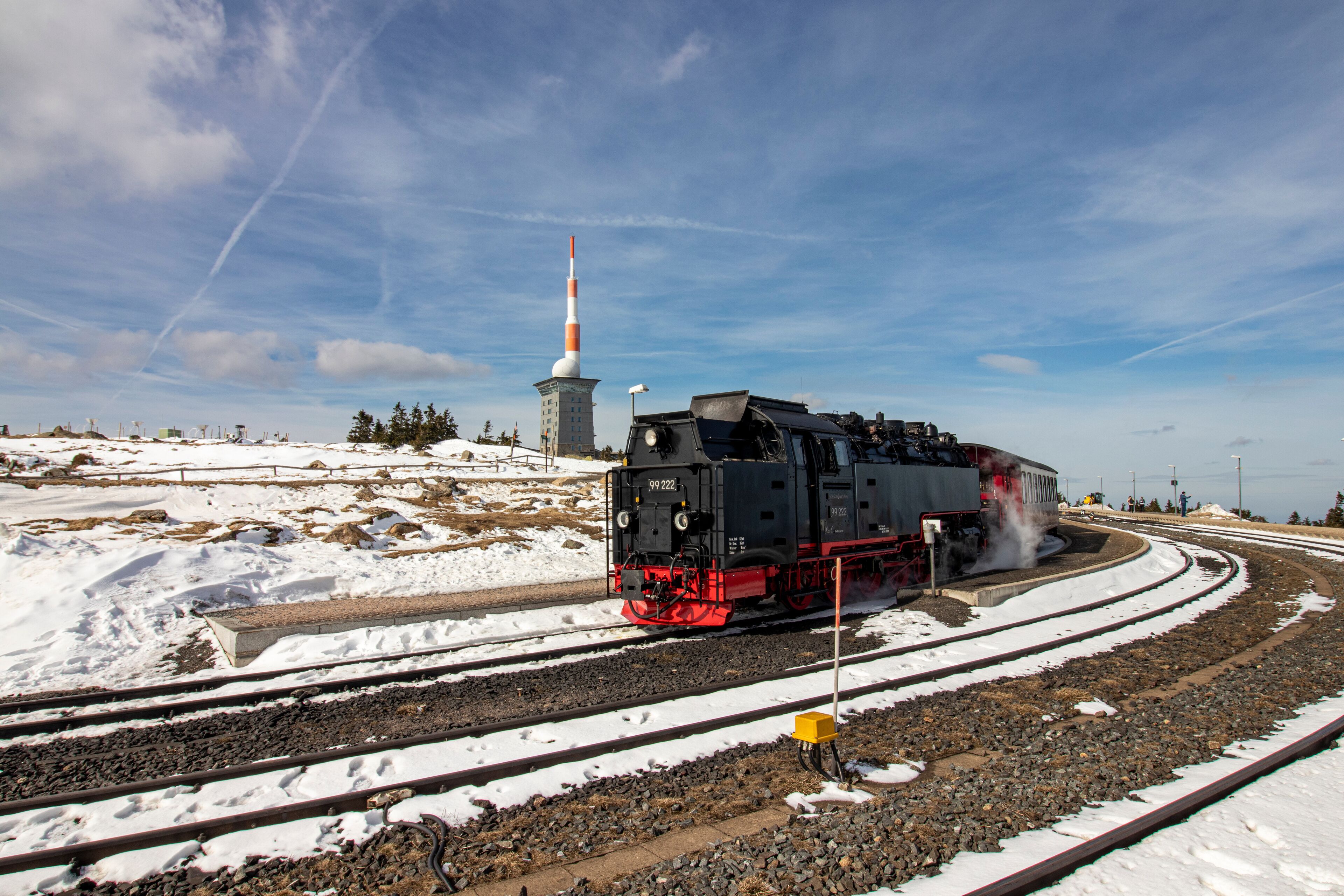 Une locomotive à vapeur sur une voie ferrée enneigée, avec une tour en arrière-plan.