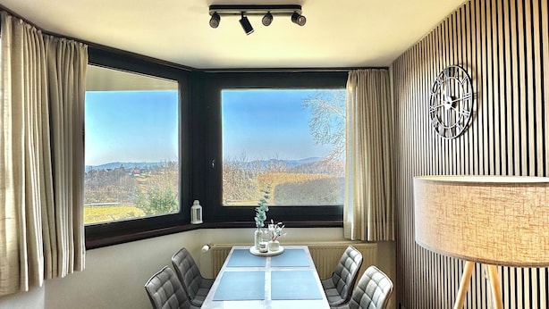 Ein Essbereich mit Tisch und Stühlen, ein Fenster mit Aussicht, eine Uhr und eine Lampe.