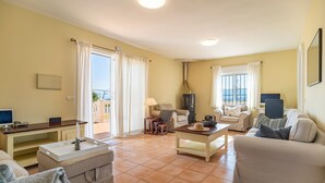 A living room with a sofa, a coffee table, a TV, and a fireplace. There is a balcony with a view of the sea. - 3 bedroom stunning home in Coin (Coin)