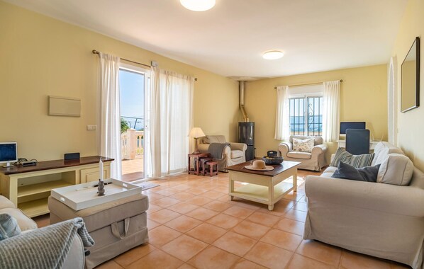Una sala de estar con sofá, mesa de centro, televisor y chimenea. Hay un balcón con vistas al mar.