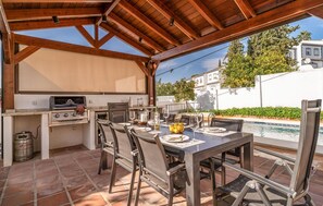 Un patio al aire libre con una parrilla, una mesa de comedor, sillas y una piscina.