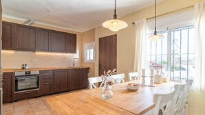 A modern kitchen with dark wooden cabinets, a built-in oven, and a wooden dining table with white chairs. - 3 bedroom stunning home in Coin (Coin)