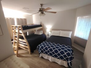 A bunk bed room with a ceiling fan, a bedside table with a lamp, and a window with curtains.